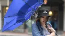 Seorang wanita membawa payungnya yang rusak saat berjalan melawan angin kencang yang ditimbulkan oleh topan Lekima di Taipei, Taiwan (9/8/2019). Topan  tersebut dinilai sebagai yang terkuat menghantam Taiwan di tahun ini. (AFP Photo/Sam Yeh)