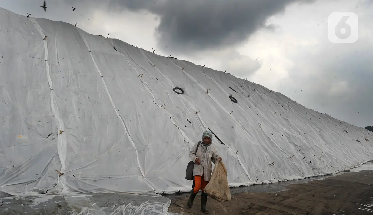 Pemulung melewati gunungan sampah yang tertutup oleh plastik putih di Tempat Pembuangan Akhir (TPA) Cipayung, Depok, Jawa Barat, Selasa (21/1/2020). Pemasangan plastik tersebut dilakukan sejak kemarin untuk mengurangi bau tak sedap di musim hujan sekaligus mengurai sampah. (merdeka.com/Arie Basuki)