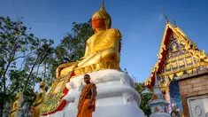 Biksu berjalan di depan patung Buddha raksasa yang mengenakan masker di kuil Wat Nithet Rat Pradit di Pathum Thani di luar Bangkok, Thailand, 12 Mei 2020. Pemasangan masker tersebut sebagai tanggapan terhadap penyebaran pandemi Covid-19. (Photo by Mladen ANTONOV / AFP)