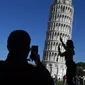 Turis berpose di depan Menara Pisa di kota Pisa, Italia pada 28 November 2018. Setelah upaya yang dilakukan selama lebih dari dua puluh tahun, para insinyur mengatakan kemiringan menara setinggi 57 meter itu telah berkurang 4 cm. (Tiziana FABI / AFP)