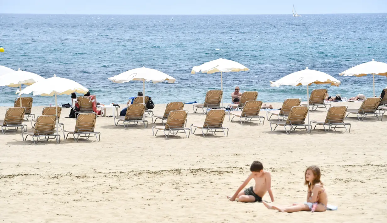 Orang-orang berjemur di Pantai Bogatell di Barcelona, Minggu (6/6/2021). Spanyol akan mengizinkan semua pelancong yang divaksinasi untuk mengunjungi negara itu mulai 7 Juni, dengan tujuan kembali menghidupkan industri perjalanan yang terpukul pandemi Covid-19. (Pau BARRENA/AFP)
