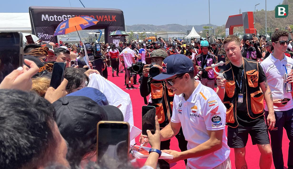 Pembalap Repsol Honda, Marc Marquez (kanan), membubuhkan tanda tangan saat menyapa penggemar dalam kegiatan MotoGP Hero Walk di Sirkuit Mandalika, Lombok , Minggu (15/10/2023). (Bola.com/Benediktus Gerendo Pradigdo)