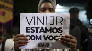Seorang perempuan memegang tanda dengan pesan yang berbunyi dalam bahasa Portugis; "Vini, kami bersamamu," saat memprotes serangan rasis yang dialami pemain Real Madrid asal Brasil, Vinicius Jr., di luar Konsulat Spanyol di Sao Paulo, Brasil, Selasa (23/5/2023). (AP Photo/Tuane Fernandes)