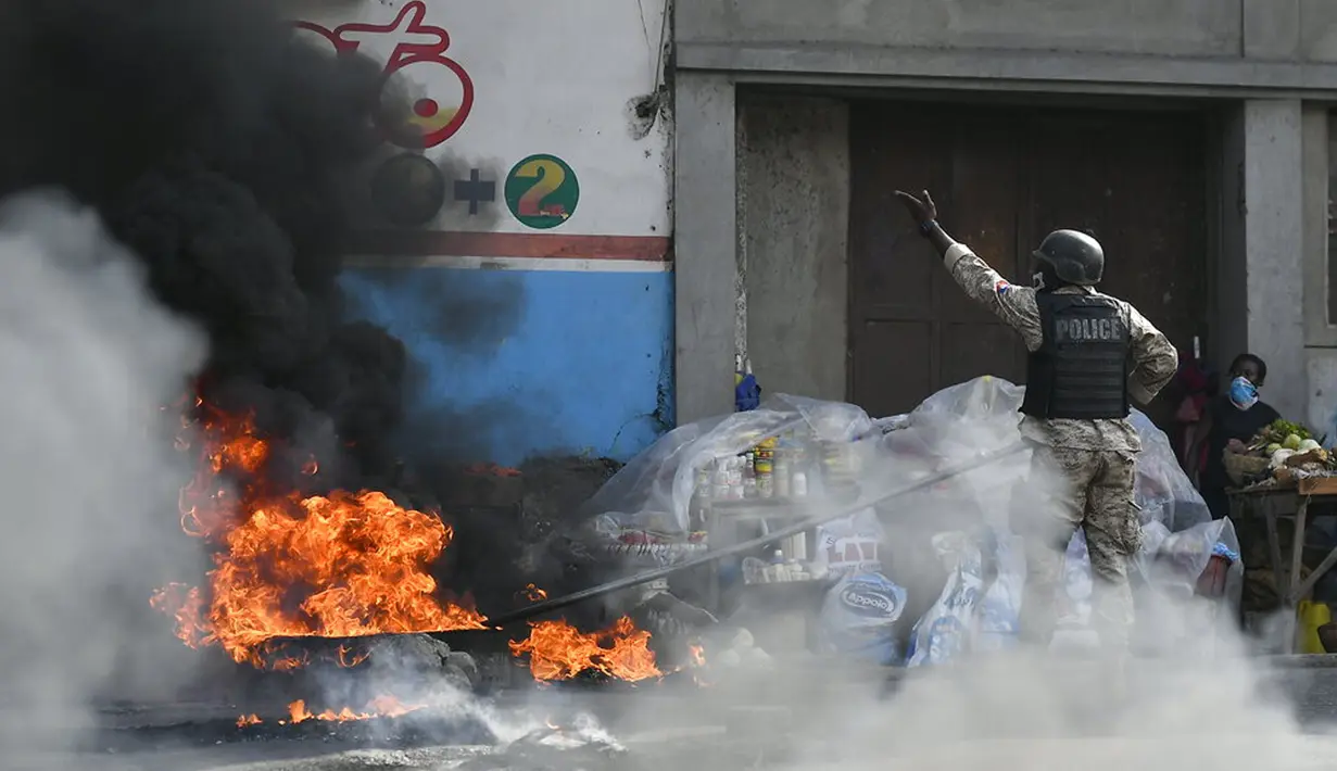 polisi mendorong ban yang terbakar ke sisi jalan agar mobil bisa lewat sat orang-orang memprotes meningkatnya kekerasan di lingkungan Lalue, Port-au-Prince, Haiti, Rabu (14/7/2021). Presiden Haiti Jovenel Moise dibunuh pada 7 Juli. (AP Photo/Matias Delacroix)