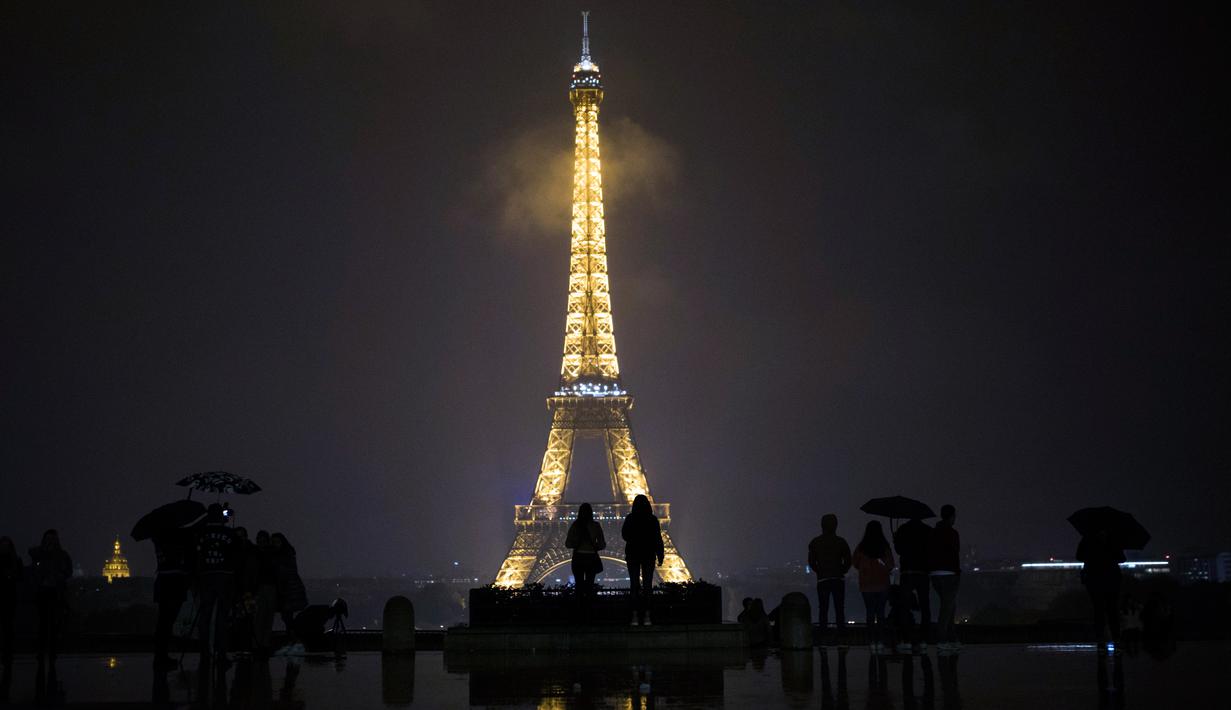 Pengunjung berkumpul di alun-alun Trocadero sebelum lampu Menara Eiffel dipadamkan di Paris, Senin (2/10). Lampu di menara yang menjadi ikon Negara Prancis ini akan dimatikan sebagai penghormatan kepada korban penembakan di Las Vegas. (AP/Kamil Zihnioglu)