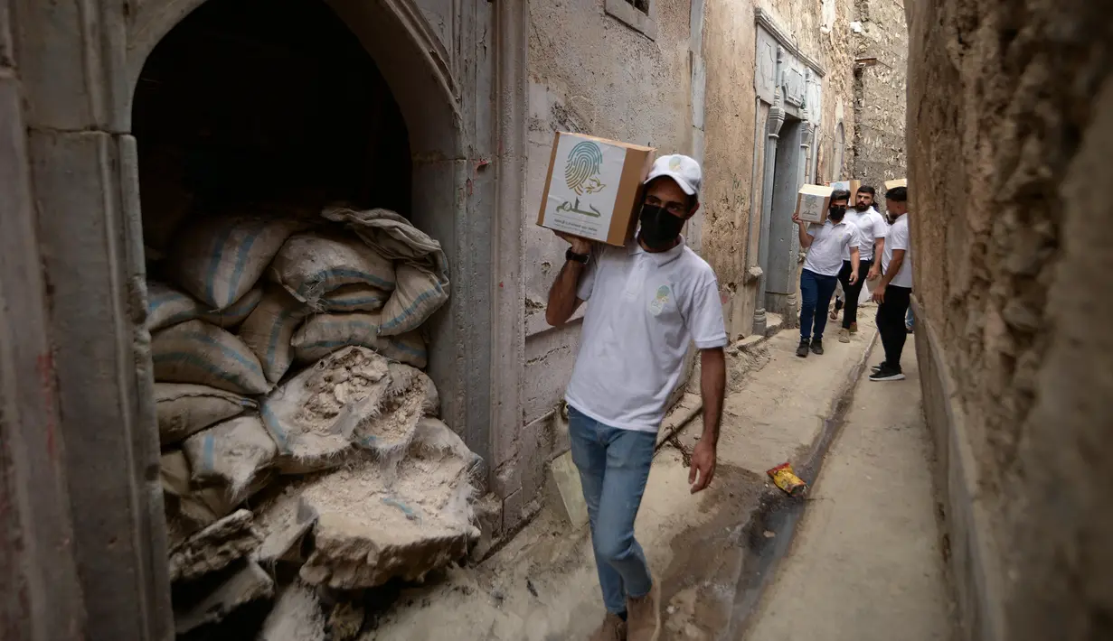 Para relawan Irak di asosiasi lokal saat mendistribusikan jatah makanan ke rumah tangga selama bulan Muslim Ramadhan di kota Mosul utara (7/5/2021). (AFP Photo/Zaid AL-Obeidi)