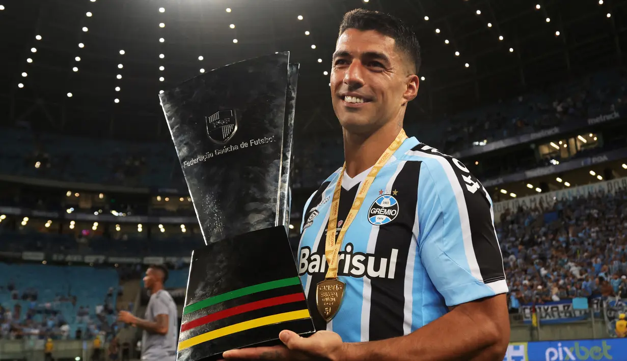 Penyerang Gremio Uruguay Luis Suarez memegang trofi setelah mengalahkan Sao Luiz pada ajang Recopa Gaucha di stadion Arena do Gremio di Porto Alegre, Brasil, Selasa (17/1/2023). (SILVIO AVILA / AFP)