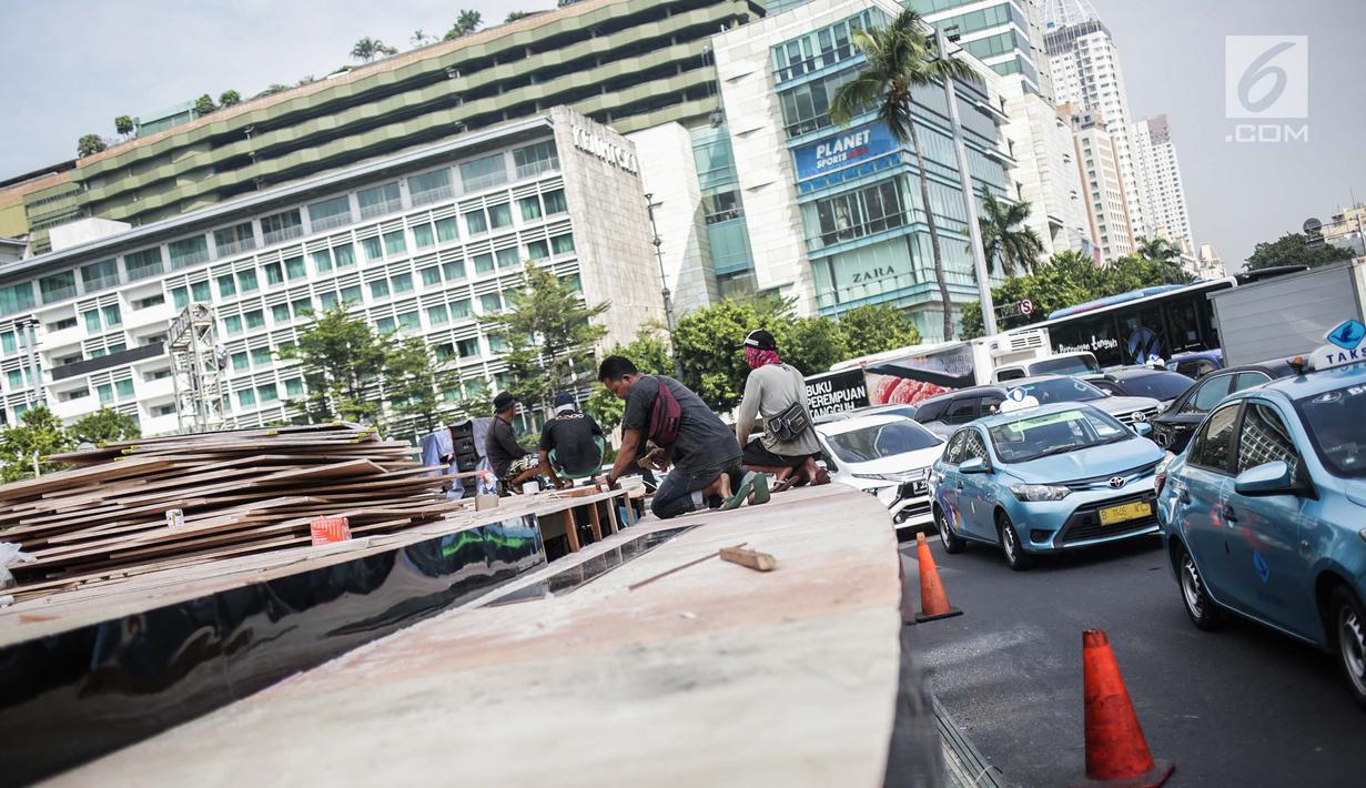 Kendaraan melintas di samping pekerja yang tengah menyelesaikan pembuatan panggung HUT ke-492 DKI di area Bundaran HI, Jakarta, Kamis (20/6/2019). Pemprov DKI Jakarta akan menggelar pesta rakyat di area Bundaran HI pada 22 Juni 2019. (Liputan6.com/Faizal Fanani)
