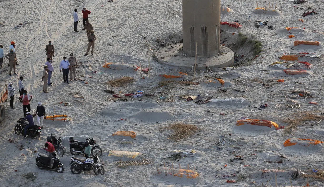 Polisi berdiri di dekat jenazah yang dimakamkan di kuburan dangkal di tepi sungai Gangga di Prayagraj, 15 Mei 2021. Polisi menjangkau penduduk desa di India utara untuk menyelidiki penemuan jasad di tepi Sungai Gangga yang memicu spekulasi mereka adalah korban COVID-19. (AP Photo/Rajesh Kumar Singh)