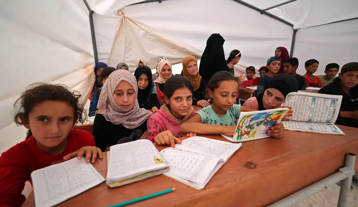 Anak-anak Suriah membuka bukunya saat mengikuti kegiatan belajar di dalam tenda yang diubah menjadi ruang kelas di kamp pengungsi di kota Maarrat Misrin di Provinsi Idlib, Suriah (6/10/2020). (AFP/Omar Haj Kadour)