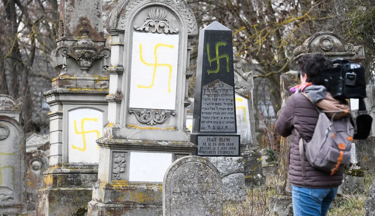 Seorang jurnalis mengambil gambar makam Yahudi yang dicoret simbol Nazi di pemakaman Yahudi, Quatzenheim, Prancis, Selasa (19/2). Prancis merupakan negara Eropa dengan komunitas Yahudi terbanyak yaitu sekitar 550 ribu orang. (Frederick FLORIN/AFP)