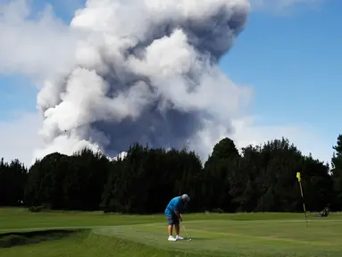 Doug Ralston bermain golf saat kepulan asap abu vulkanik berembus dari puncak gunung Kiluaea di Volcano, Hawaii (21/5). Lava dari gunung Kilauea Hawaii mengalir ke laut dan memicu reaksi kimia yang menciptakan asap hitam. (AP Photo/Jae C. Hong)