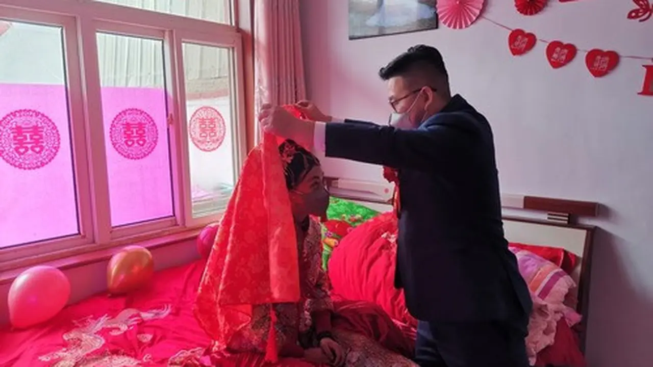 Zhang Long mengangkat kain merah penutup wajah sang mempelai wanita, Chen Xiao, saat pernikahan mereka pada 6 Februari 2020. (Xinhua)