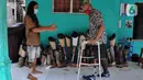 Ronald Regen (33), perajin yang juga penyandang disabilitas membantu pelanggan mencoba kaki palsu di Dusun IV Rawailat, Desa Dayeuh, Cileungsi, Bogor, Selasa (29/3/2022). Dia berharap pemerintah membantu 200 penyandang disabilitas sekitar Bogor yang belum punya kaki palsu. (merdeka.com/Arie Basuki)