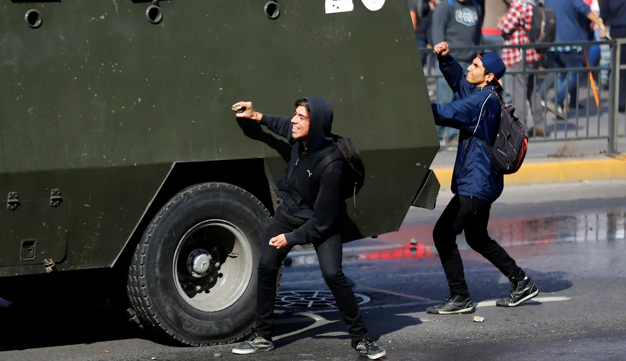 Sejumlah pelajar membawa batu untuk merusak kendaraan polisi yang terparkir dijalan, Santiago , Chile , 21 April 2016. Sejumlah pelajar nekat melempari polisi dengan batu dan bom rakitan. (REUTERS / Clemente Villavicencio)