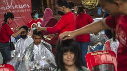 Penata rambut melakukan cukur rambut gratis saat acara amal di Surabaya, Jawa Timur, Senin (8/11/2021). Layanan cukur rambut gratis ini dilakukan kepada 100 anak yatim piatu. (Juni Kriswanto/AFP)