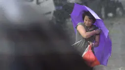 Seorang wanita memegang payung saat berjalan di tengah hembusan Topan Kalmaegi yang menerjang wilayah Qionghai di provinsi Hainan, Tiongkok, (16/9/2014). (REUTERS/Stringer)