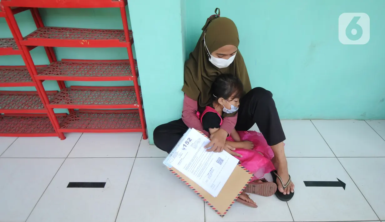 Warga bersama anaknya menunggu giliran untuk mengambil uang Bantuan Sosial Tunai (BST) di SDN Pondok Cabe Udik 03, Tangerang Selatan, Rabu (28/07/2021). Lebih dari dari 1800 warga mendapatkan BST yang dirapel dua bulan sekaligus dengan total Rp600ribu. (merdeka.com/Arie Basuki)