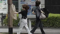 Orang-orang berjalan di tengah hujan badai yang dibawa oleh Badai Tropis Khanun di Kagoshima, Jepang selatan Rabu, 9 Agustus 2023. (Kyodo News via AP)
