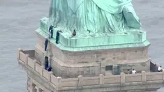 Petugas kepolisian membujuk seorang wanita yang memanjat Patung Liberty di New York, Rabu (4/7). Aksi wanita bernama Therese Okoumou ini memprotes kebijakan imigrasi pemerintah Presiden Donald Trump yang memisahkan keluarga migran. (AFP/PIX11 News/HO)