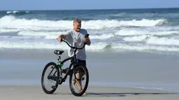 Seorang pria melihat ponselnya saat bersepeda di Jacksonville Beach, Florida (17/4/2020). Walikota Jacksonville, Lenny Curry, Kamis mengumumkan bahwa pantai-pantai Duval County akan dibuka pukul 5 sore. (Sam Greenwood / Getty Images / AFP)