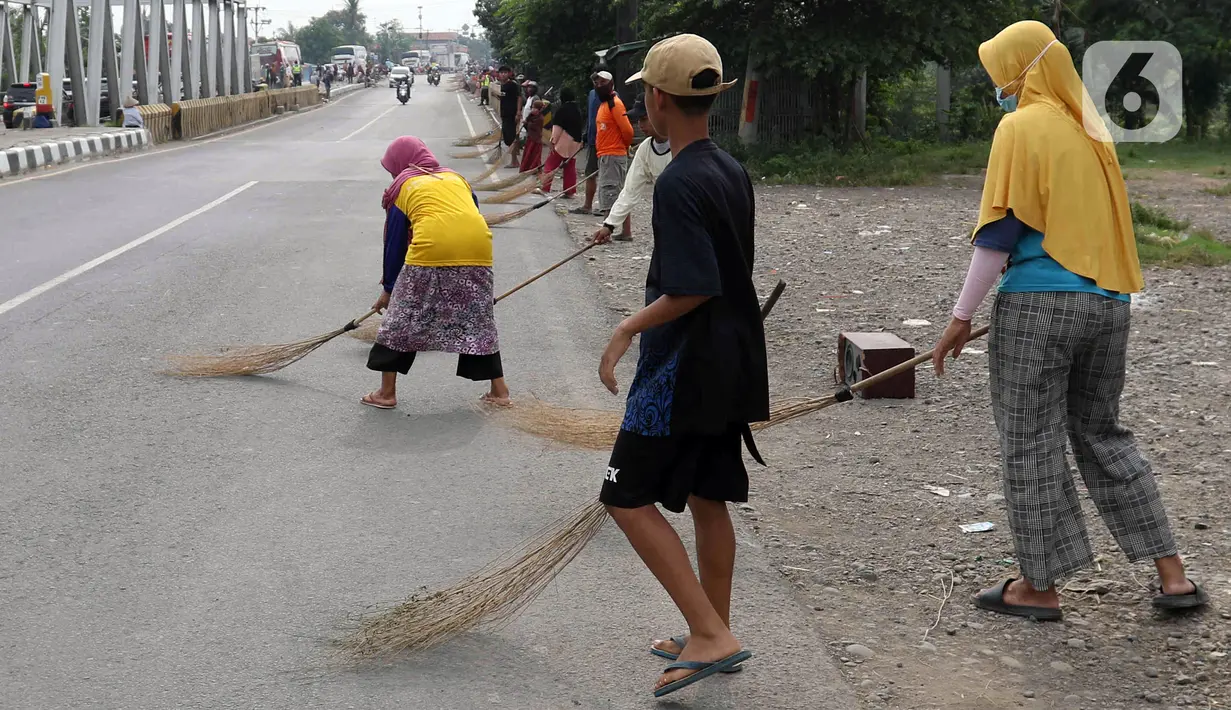 <p>Sejumlah warga menunggu kendaraan bermotor memberi sedekah dengan melempar uang di kawasan Jembatan Sewo, Indramayu, Jawa Barat, Jumat (29/4/2022). Aksi mengambil uang sedekah menggunakan sapu meningkat saat puncak arus mudik. (Liputan6.com/Herman Zakharia)</p>