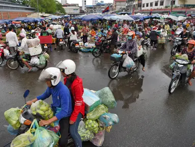 Orang-orang mengendarai sepeda motor melewati pasar di Phnom Penh (24/7/2020). Pasar membentuk bagian integral dalam kehidupan orang Kamboja, dengan kunjungan harian yang dilakukan untuk persediaan makanan untuk hari itu serta barang-barang lainnya. (AFP/Tang Chhin Sothy)