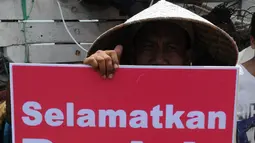 Seorang nelayan menunjukkan poster berisi penolakan terhadap proyek reklamasi Teluk Jakarta saat upacara sedekah bumi yang lebih dikenal dengan sebutan Nadran di Muara Angke, Jakarta, Minggu (13/12/2015). (Liputan6.com/Helmi Afandi)