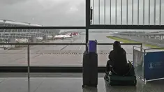 Seorang calon penumpang duduk di kopernya mengamati pesawat yang diparkir di landasan setelah semua penerbangan dibatalkan di Bandara Internasional Pudong, Shanghai, Minggu (25/7/2021). Ratusan jadwal penerbangan dibatalkan saat topan In-Fa bergerak menuju mendarat. (AP Photo/Andy Wong)