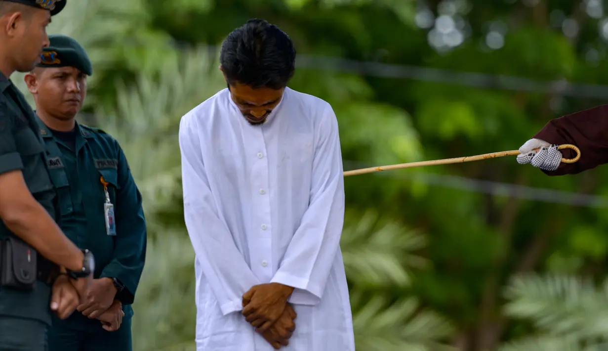 Seorang pria menjalani hukuman cambuk di depan umum oleh anggota polisi Syariah di Banda Aceh, Senin (21/10/2019). Pria berprofesi sopir itu dikenakan 6 kali sabetan cambuk setelah dipotong masa tahanan dua kali cambuk karena terbukti melakukan perbuatan maisir (judi). (CHAIDEER MAHYUDDIN / AFP)