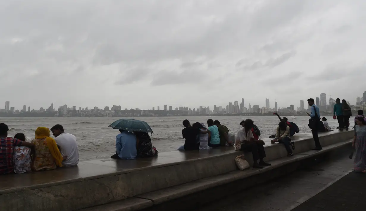 Warga India duduk di pinggir laut ketika awan gelap menyelimuti langit Mumbai (12/6/2019). Badai siklon vayu melesat ke arah barat India telah diperkuat dengan hembusan angin hingga 170 kilometer per jam (105 mph) yang diperkirakan akan menerjang pada 13 Juni 2019. (AFP Photo/Punit Paranjpe)