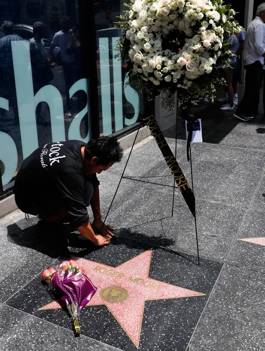Pekerja meletakkan karangan bunga dekat bintang Walk of Fame milik aktor Inggris, Roger Moore, di Hollywood, Los Angeles, Selasa (23/5). Aktor yang namanya dikenal karena memerankan James Bond itu meninggal dunia pada usia 89 tahun. (AP Photo/Jae C. Hong)
