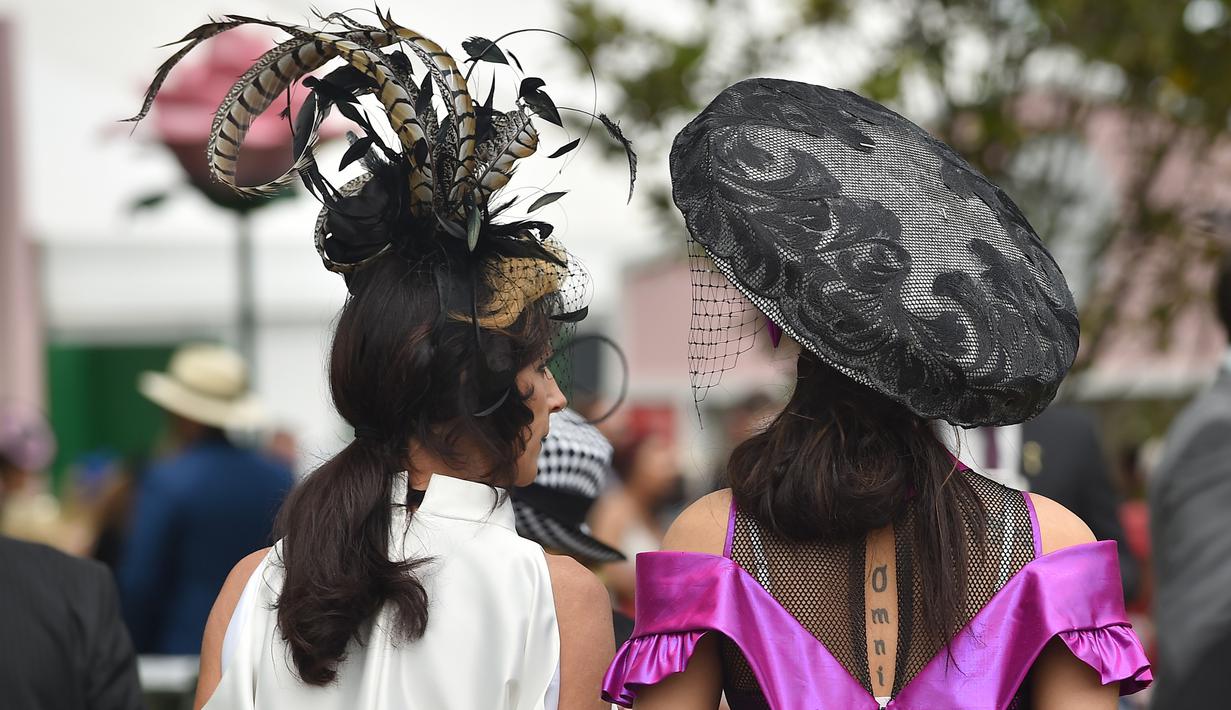 Dua orang wanita berjalan memakai hiasan kepala saat menyaksikan kompetisi balap kuda Melbourne di arena pacuan kuda Flemington Racecourse di Melbourne, Australia (1/11). Balap kuda ini diselenggarakan pertama kalinya pada tahun 1861. (AFP/Paul Crock)