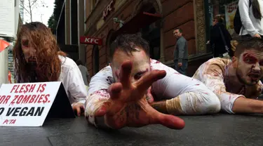 Pejalan kaki mengamati aktivis PETA yang berdandan menyerupai zombie sambil berbaring di jalan depan sebuah restoran cepat saji di Sydney, Kamis (15/6). Aksi itu sebagai bentuk protes terhadap konsumsi daging dan mempromosikan vegetarian (SAEED KHAN/AFP) 