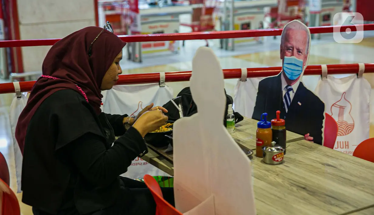 Pengunjung menikmati makanan di meja yang diberi pembatas banner bergambar Presiden AS Joe Biden di Restoran Hulu Hulu, Mall Kuningan City, Jakarta, Senin (1/3/2021). Banner bergambar tersebut berguna untuk pembatas bagi pengunjung yang makan di tempat saat pandemi. (Liputan6.com/Faizal Fanani)