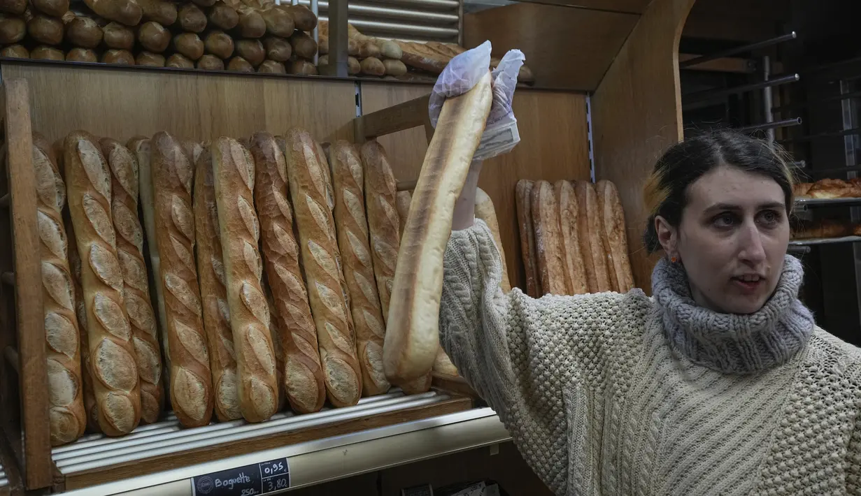Mylene Poirier berbicara dengan seorang pelanggan saat dia mengambil baguette di sebuah toko roti, di Versailles, sebelah barat Paris, Selasa, 29 November 2022. Badan PBB memberikan status warisan budaya takbenda pada tradisi pembuatan baguette dan gaya hidup yang mengelilinginya. (AP Photo/Michel Euler)