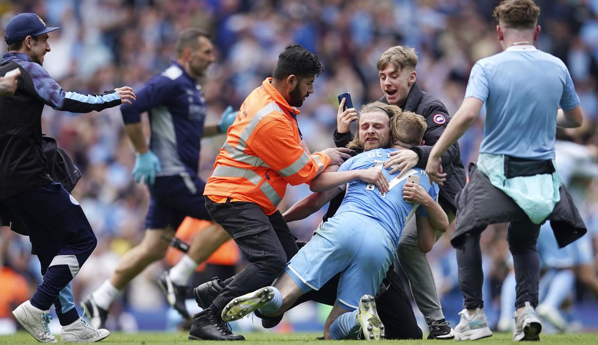 Para suporter tampak memeluk pemain Manchester City, Kevin De Bruyne, saat merayakan gelar juara Liga Inggris 2021 / 2022 di Stadion Etihad, Minggu (23/5/2022). (AP/Dave Thompson)