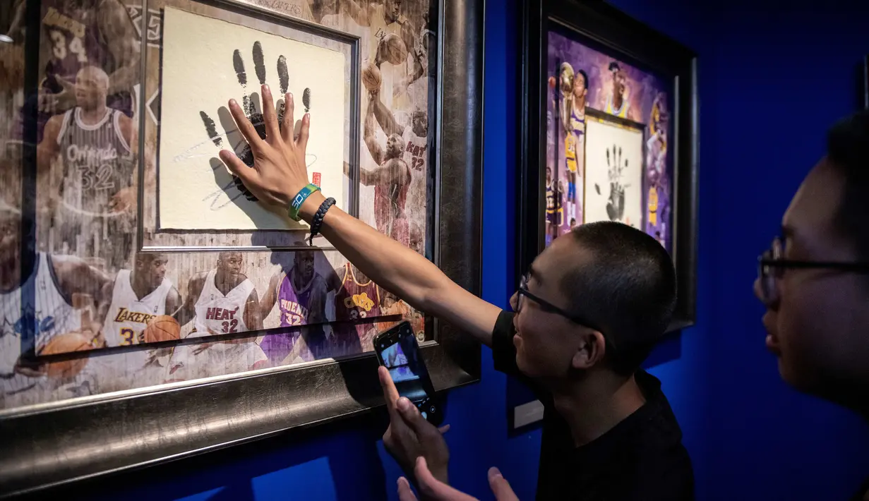 Pengunjung meletakkan tangannya di atas cap tangan Shaquille O'Neal dalam pameran NBA (National Basketball Association) di Beijing, China, Senin (19/8/2019). (NICOLAS ASFOURI/AFP)