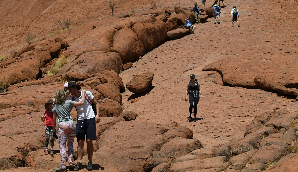 Wisatawan mendaki Uluru yang juga dikenal sebagai Batu Ayers di Taman Nasional Uluru-Kata Tjuta, utara Australia, Jumat (25/10/2019). Kawasan wisata bukit batu Uluru dipenuhi pengunjung, lantaran hari ini merupakan hari terakhir sebelum larangan pendakian diberlakukan. (SAEED KHAN / AFP)