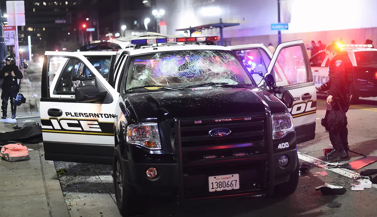 Petugas memeriksa kendaraan polisi yang dirusak pengunjuk rasa di Oakland, California, Rabu (9/11). Sebagian warga AS turun ke jalan-jalan di seluruh wilayah Amerika Serikat tak terima dengan kemenangan Donald Trump dalam Pilpres AS. (REUTERS/Noah Berger)