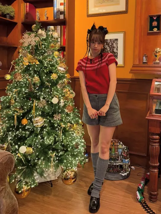 Hyeri berfoto dengan pohon Natal setinggi dirinya yang dihiasi ornamen gold. Ia mengenakan atasan  knit merah lengan pendek dipadukan celana pendek abu-abu senada dengan kaos kakinya. [@hyeri_0609]