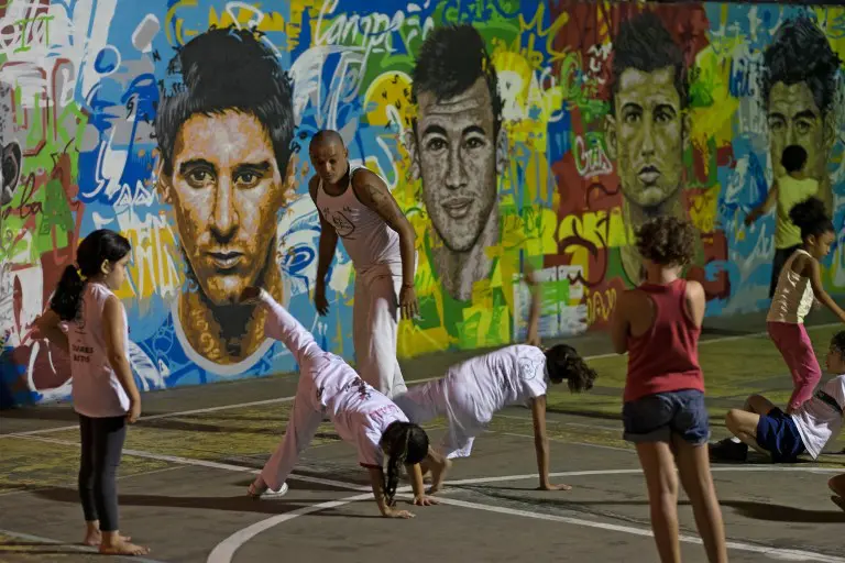 Seorang pelatih sedang memperhatikan anak didiknya melakukan gerakan Capoeira di dekat tembok lukisan wajah pemain top dunia, Brasil, Rabu (21/05/2014) (AFP PHOTO/Yasuyoshi CHIBA).