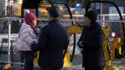 Sepasang suami istri menonton seorang anak bermain di ranjang yang memantul di sebuah taman hiburan di Beijing (17/1/2022).  Partai Komunis yang berkuasa khawatir fakta ini bisa menghalangi ambisi mereka untuk meningkatkan kekayaan nasional dan pengaruh global. (AP Photo/Andy Wong)