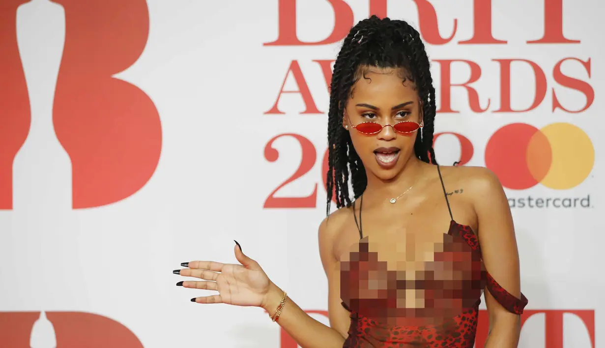 Diana De Brito, yang dikenal sebagai IAMDDB berpose di karpet merah saat tiba menghadiri BRIT Awards 2018 di London, Inggris (21/2). Rapper asal Inggris ini tampil seksi dengan busana transparan sambil membawa mawar berwarna putih. (AFP Photo/Tolga Akmen)