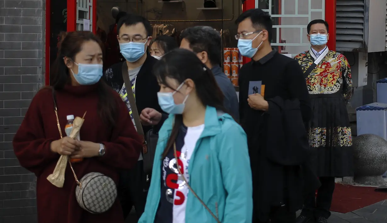 Seorang pekerja mengenakan masker untuk mencegah penyebaran virus corona berdiri menyaksikan turis bertopeng berjalan di dekat toko suvenirnya di Beijing (25/10/2020). (AP Photo/Andy Wong)