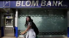 Seorang perempuan melintas di sebuah cabang Bank BLOM yang tutup di Beirut, Lebanon, Selasa (20/9/2022). Ketika cabang bank dibuka kembali, sejumlah bank merencanakan langkah-langkah perlindungan diri yang ketat. Dimana, seluruh nasabah diperiksa dan hanya menerima mereka yang memiliki janji temu terjadwal. (AP Photo/Hassan Ammar)