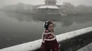 Seorang wanita mengenakan kostum tradisional berpose di dekat Kota Terlarang saat salju turun di Beijing, China (18/3/2022). Sebagian besar distrik di ibu kota China, Beijing, mengalami salju pada hari Kamis, dengan distrik paling utara Yanqing melaporkan hujan salju terberat. (AP Photo/Ng Han Guan)