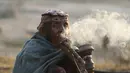 Seorang wanita nomaden merokok hukka, atau gelembung hubble, saat kelompok mereka berhenti sementara di jalan raya Jammu-Srinagar di Nagrota, di pinggiran Jammu, India, Selasa (9/11/2021). Anggota suku tersebut pindah dari perbukitan untuk menghindari musim dingin. (AP Photo/Channi Anand)