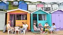 Orang-orang duduk di luar gubuk pantai di Walton-on-the-Naze, di Inggris pada 15 Juli 2021. Gubuk kayu yang dicat cerah berjajar di garis pantai Inggris telah menikmati booming selama pandemi, ketika orang-orang menemukan kembali tempat istirahat di tepi pantai di dekat rumah. (Justin TALLIS/AFP)