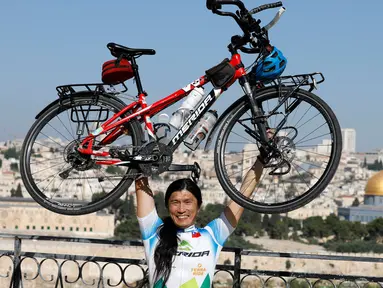 Pria Taiwan, Jacky Chen (40), berpose mengangkat sepedanya di Bukit Zaitun yang menghadap ke Kota Tua Yerusalem dan Kubah Batu pada 10 Juni 2019. Mantan teknisi elektronik itu berhenti dari pekerjaannya demi mewujudkan impiannya berkeliling dunia dengan sepeda. (MENAHEM KAHANA/AFP)